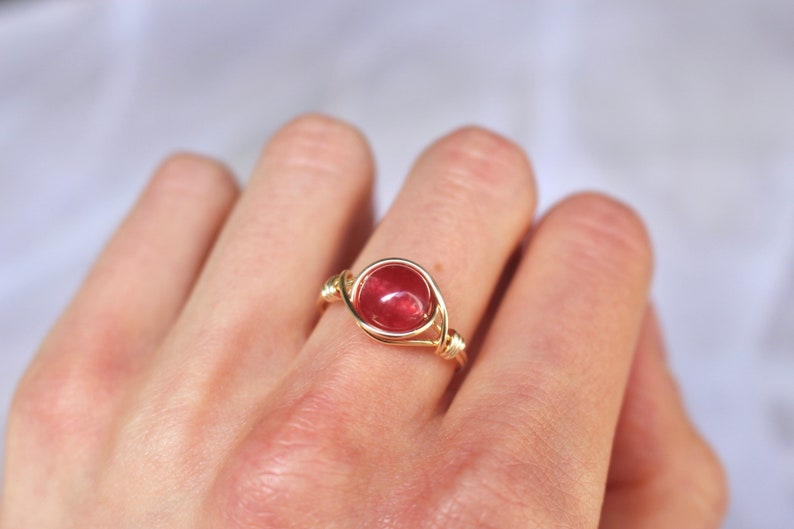 May include: A gold wire wrapped ring with a round, red gemstone.