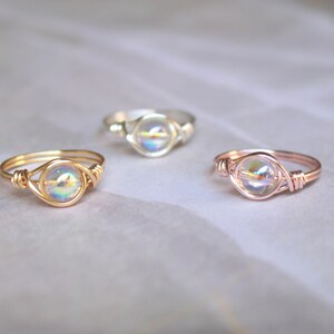 Pu&ograve; includere: Tre anelli con perline di vetro iridescenti incastonate in filo d'oro, oro rosa e argento.