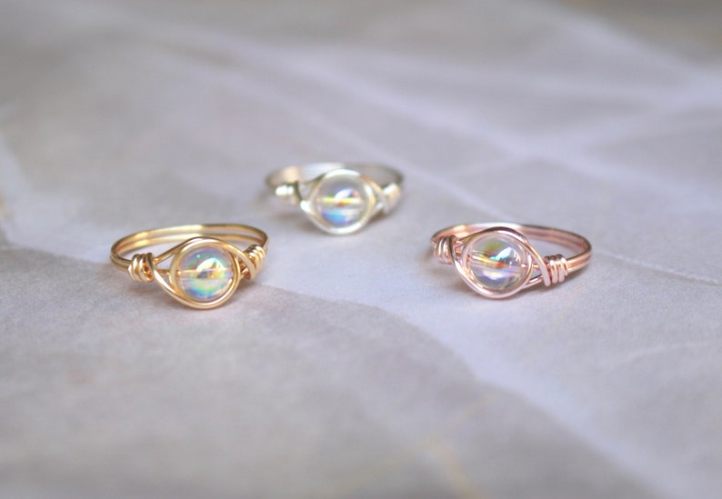 Pu&ograve; includere: Tre anelli con perline di vetro iridescenti incastonate in filo d'oro, oro rosa e argento.