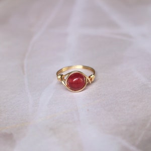May include: A gold wire wrapped ring with a red gemstone.