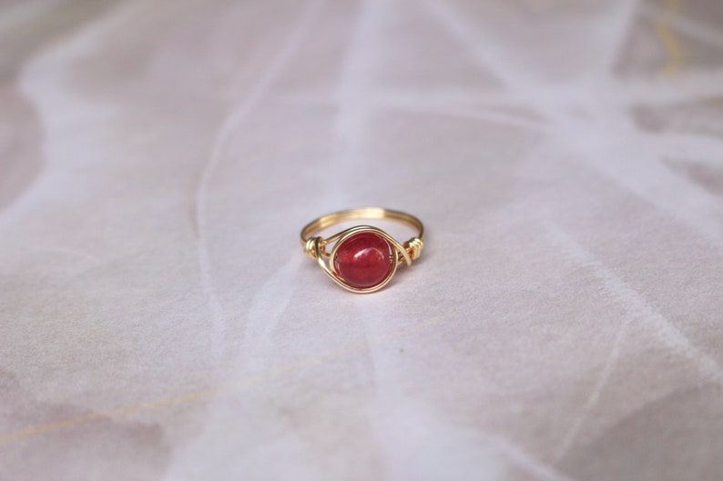 May include: A gold wire wrapped ring with a red gemstone.