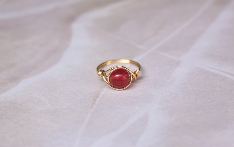 May include: A gold wire wrapped ring with a red gemstone.