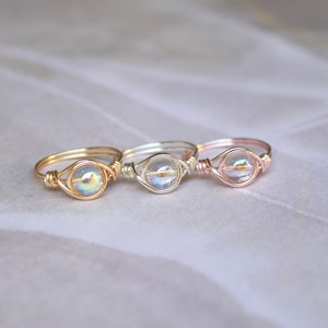 Pu&ograve; includere: Tre anelli avvolti in filo con perline di vetro iridescenti. Gli anelli sono in oro, argento e oro rosa.