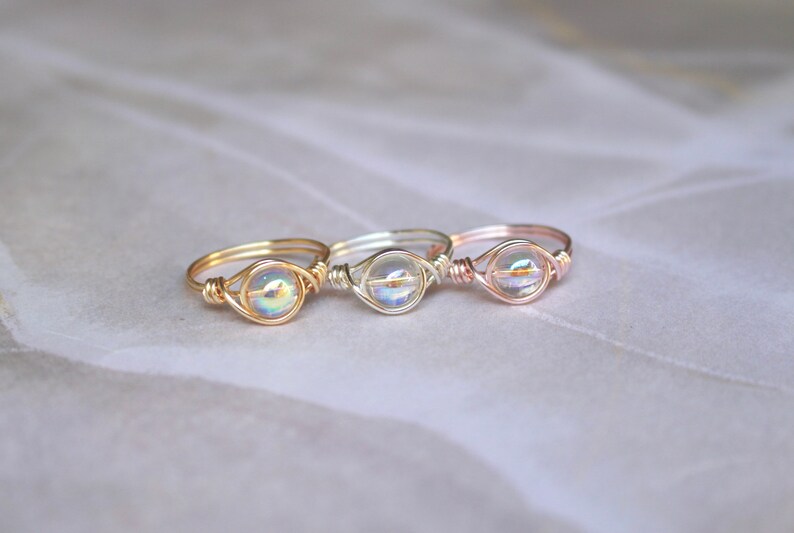 Pu&ograve; includere: Tre anelli avvolti in filo con perline di vetro iridescenti. Gli anelli sono in oro, argento e oro rosa.