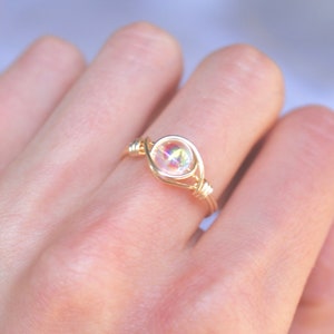 Pu&ograve; includere: Un anello avvolto in filo d'oro con una pietra preziosa trasparente e iridescente.
