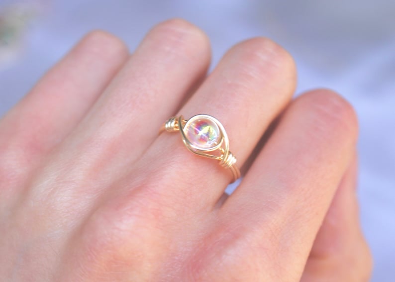 Pu&ograve; includere: Un anello avvolto in filo d'oro con una pietra preziosa trasparente e iridescente.