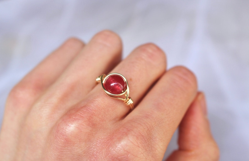 May include: A gold wire wrapped ring with a red gemstone.