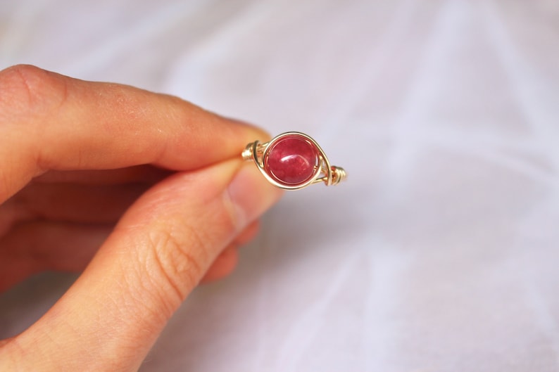May include: A gold wire wrapped ring with a red gemstone.