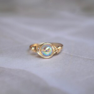 Pu&ograve; includere: Un anello avvolto in filo d'oro con una perla rotonda iridescente al centro.
