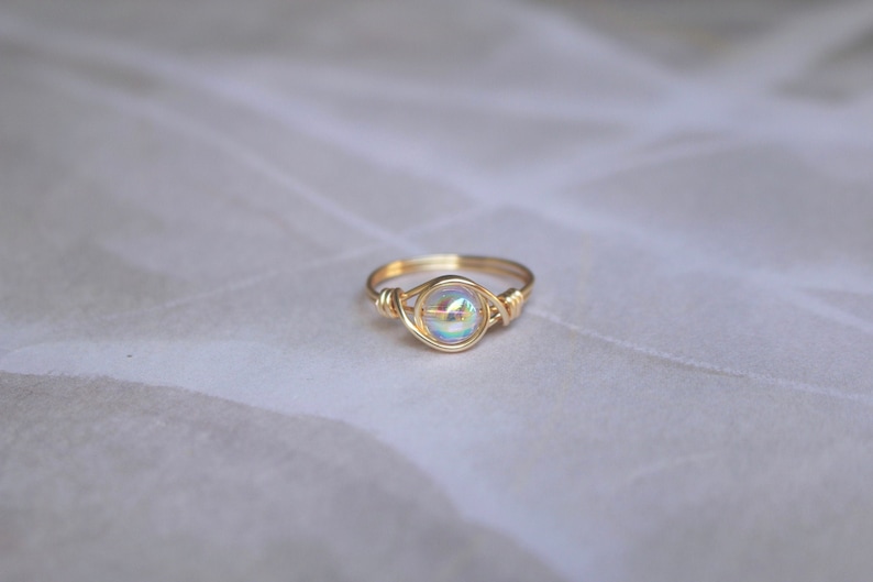 Pu&ograve; includere: Un anello di filo d'oro con una pietra preziosa bianca iridescente.