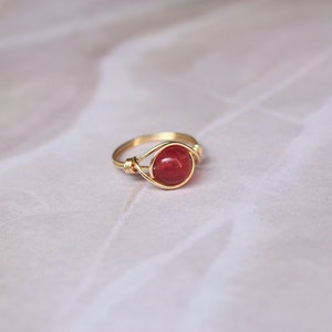 May include: A gold wire wrapped ring with a red gemstone.