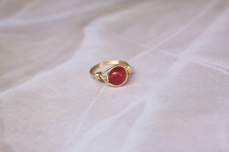 May include: A gold wire wrapped ring with a red gemstone.