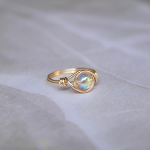 Pu&ograve; includere: Un anello in filo d'oro con una pietra rotonda iridescente.