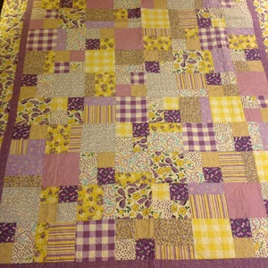 May include: A patchwork quilt with a variety of yellow and purple floral patterns. The quilt is made up of squares and rectangles of different sizes and colors.