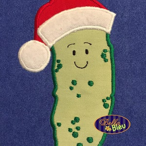 May include: A green pickle wearing a red and white Santa hat with a white pom-pom. The pickle has a smiling face with green eyes and a green mouth.
