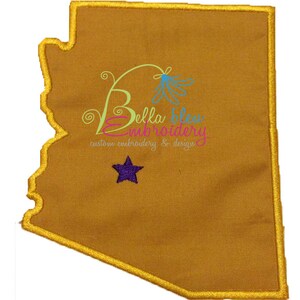 May include: A gold outline of the state of Arizona with a purple star in the center. The text "Bella Bleu Embroidery" is written in a cursive font with a blue flower design. The text "custom embroidery & design" is written below the company name.