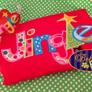 May include: A red shirt with the word "Jingle" embroidered in colorful letters with polka dots. A matching headband with the word "Jingle" is also included. The shirt and headband are both decorated with a star and a Christmas tree.
