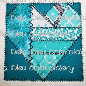 Può includere: Un cuore a patchwork blu turchese con cuciture nere. Il cuore è fatto di diversi tessuti con vari motivi, tra cui un tessuto bianco con un motivo floreale blu turchese. Il testo "Bella Bleu Embroidery" è visibile sul cuore.
