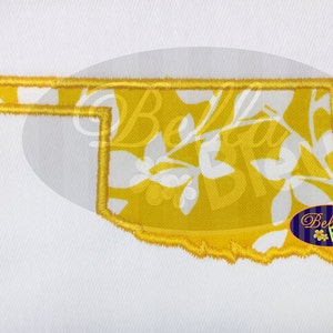 May include: Yellow embroidered outline of the state of Oklahoma with a white floral pattern inside. The outline is stitched with a yellow thread. The floral pattern is a repeating design of white leaves on a yellow background.