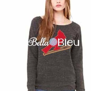 Può includere: Una felpa a maniche lunghe color antracite con una grafica di un cardinale rosso e una mazza da baseball. Il testo "Bella Bleu" è stampato sulla parte anteriore della felpa.
