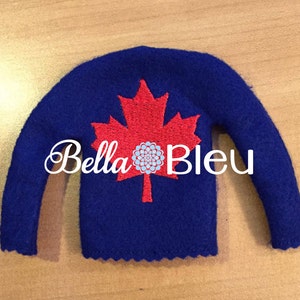 Puede incluir: Un suéter de fieltro azul para elfo con una hoja de arce roja bordada y el texto "Bella Bleu".