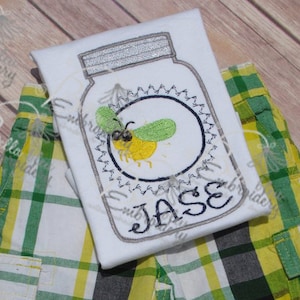 May include: White t-shirt with an embroidered design of a mason jar with a firefly inside. The name "Jase" is embroidered below the jar.