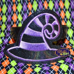 May include: A black and purple witch hat headband with glitter. The hat has a curled brim and a purple stripe design. The headband is on a black and white checked fabric.