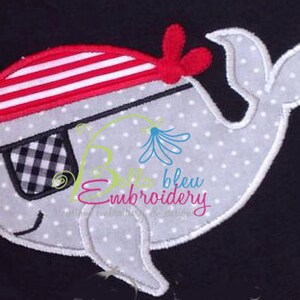 May include: A gray whale with a red and white striped pirate hat and a black and white checkered eye patch. The whale is embroidered on a dark blue fabric.