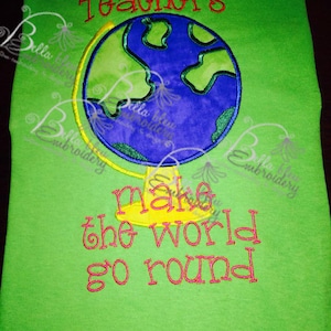 May include: Green t-shirt with embroidered text that reads "Teachers make the world go round". The text is in red and pink. There is a yellow and blue embroidered globe in the center of the shirt.
