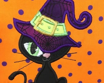 Puede incluir: Un gato negro con un sombrero de bruja morado con un diseño de telaraña y una hebilla dorada. El gato está sentado sobre un fondo naranja con lunares morados.