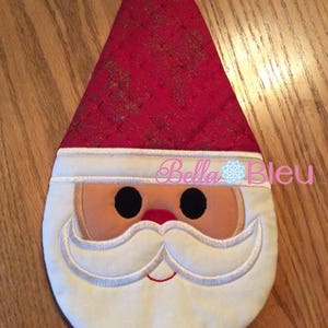 May include: A red and white Santa Claus face pot holder with a white beard and black eyes. The pot holder is quilted and has a gold glitter design.