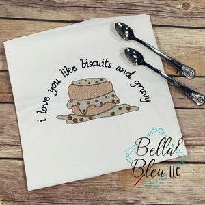 May include: White kitchen towel with embroidered text "I love you like biscuits and gravy" and a brown and white illustration of biscuits and gravy.