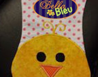 May include: A pink and white fabric baby bib with a yellow chick design and the text "Bella Bleu" embroidered in blue and orange.