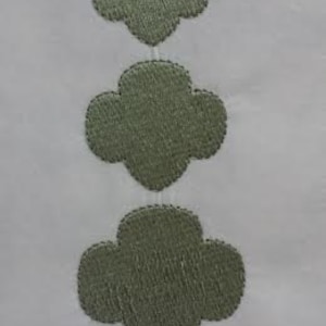 May include: Three green embroidered clover shapes in a vertical row on a white background.