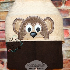 May include: A brown and beige knit hat with a brown monkey face embroidered on the front. The hat has a brown fleece lining. The text "yourpursenality - embroidery & vinyl for all "pursenalities" is printed on the hat.