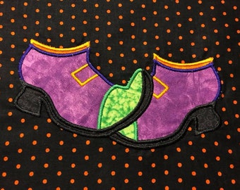 May include: Two purple witch shoes with green and orange accents on a black background with orange polka dots.