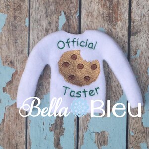 May include: White elf-sized sweater with embroidered cookie and text "Official Taster".