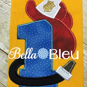 Può includere: Un numero uno blu e nero con pois bianchi, un cappello da pompiere rosso e un tubo nero. Il design è su uno sfondo di tessuto giallo. Il testo "Bella Bleu" è visibile sotto il numero.