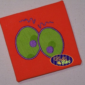 May include: Orange fabric with two large green eyes with purple pupils and a small purple "Bella Bleu" logo in the bottom right corner.