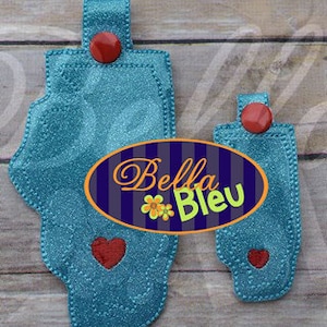 Puede incluir: Dos llaveros de tela azul con detalles en forma de corazón rojo y un botón rojo. El llavero más grande tiene forma de pie. El llavero más pequeño es un rectángulo. Los llaveros están etiquetados como "Bella Bleu".