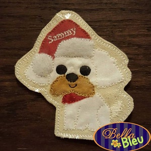 Puede incluir: Aplique de fieltro blanco de un perro con un gorro de Papá Noel rojo con el nombre "Sammy" bordado. El perro lleva una bufanda roja y tiene ojos marrones y una nariz marrón.
