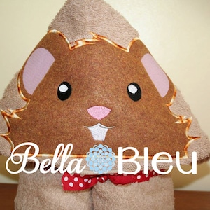 May include: A brown hooded towel with a brown and pink embroidered hamster face. The towel has a red and white polka dot bow tie and the text "Bella Bleu" embroidered on the front.