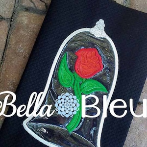 May include: A black fabric pouch with a white embroidered design of a red rose inside a glass dome. The text "Bella Bleu" is visible on the pouch.