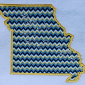 May include: A yellow outline of the state of Missouri with a blue and yellow chevron pattern inside.