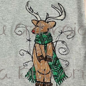 May include: Embroidered design of a reindeer wearing a green scarf with a red nose. The reindeer is standing in front of a brown branch with white snow on the ground.
