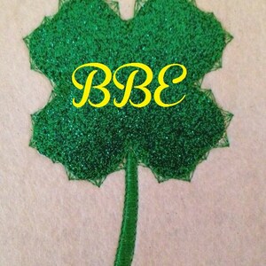 Peut inclure: Un trèfle vert pailleté avec un monogramme brodé jaune "BBE" au centre.