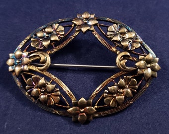 May include: A gold-toned oval brooch with a delicate filigree design featuring stylized flowers. The brooch has a pin back.