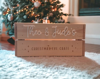 May include: A light-colored wooden crate with the words "Theo & Jude's" and "Christmas Eve Crate" in white lettering. The crate is sitting on a white rug in front of a Christmas tree.
