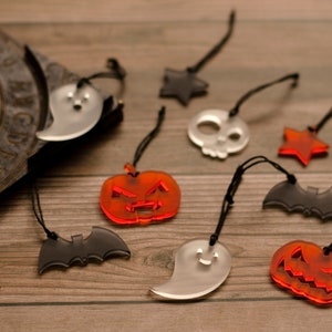 May include: A collection of nine Halloween-themed ornaments, including ghosts, bats, pumpkins, stars, and a skull. The ornaments are made of clear acrylic and have a variety of colours, including black, white, orange, and red.