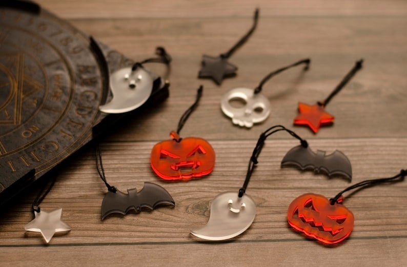 May include: A collection of nine Halloween-themed ornaments, including ghosts, bats, pumpkins, stars, and a skull. The ornaments are made of clear acrylic and have a variety of colours, including black, white, orange, and red.